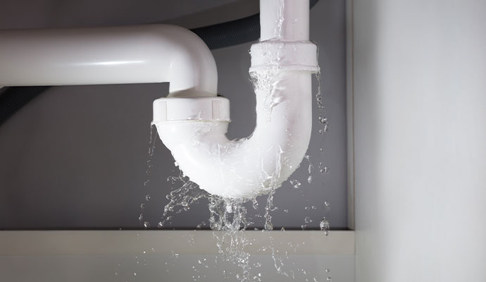 White PVC P-trap drain pipe under a sink with water spraying out