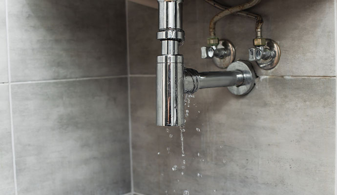 Water dripping from a chrome P-trap pipe underneath a bathroom sink