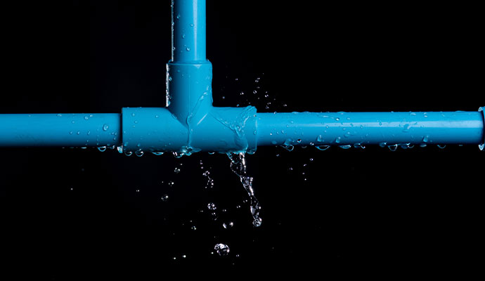 Water spraying and dripping from a cracked joint in a blue PVC plumbing pipe